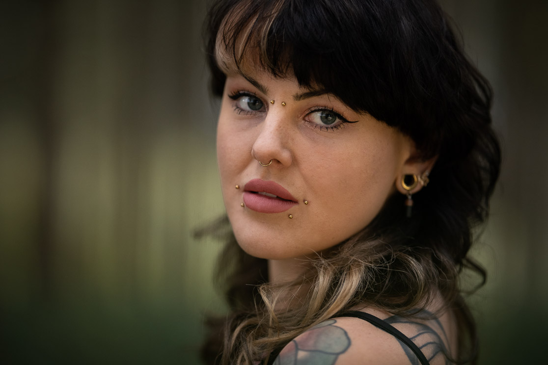 Portrait einer Frau mit Tattoos vor grünem Waldhintergrund